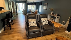 A spacious living room with a dark leather sofa set, wooden coffee table, and a dining area with a chandelier. - Incredible KY Lake Waterfront Home with Dock (Gilbertsville)