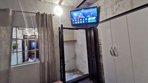 A room with a television mounted on the wall, a window with curtains, a door, and a wooden floor. - Beautiful apartment in the city center (Arequipa)