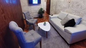 A living room with a grey sofa, a matching armchair, a small white table, and a television mounted on the wall. - Beautiful apartment in the city center (Arequipa)