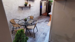 A small outdoor patio with a round glass table and wicker chairs, surrounded by a white wall with hanging lights and a potted plant. - Beautiful apartment in the city center (Arequipa)
