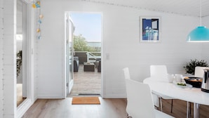 A modern kitchen with white cabinetry, a dining area with white chairs, a blue pendant light, and a view of the outdoor patio. - Pet friendly home in Bogø By with WiFi (Bogø By)