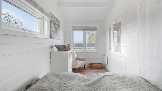 A narrow, white-walled room with a bed, a chair, and a window with a view of the outdoors. - Pet friendly home in Bogø By with WiFi (Bogø By)