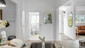 A modern kitchen with white wooden walls, a stainless steel sink, and a dining area with a brown leather couch. - Pet friendly home in Bogø By with WiFi (Bogø By)