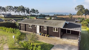 A single-story house with a dark exterior, a tiled roof, and a small porch. It is surrounded by a well-maintained lawn and a few potted plants. - Pet friendly home in Bogø By with WiFi (Bogø By)