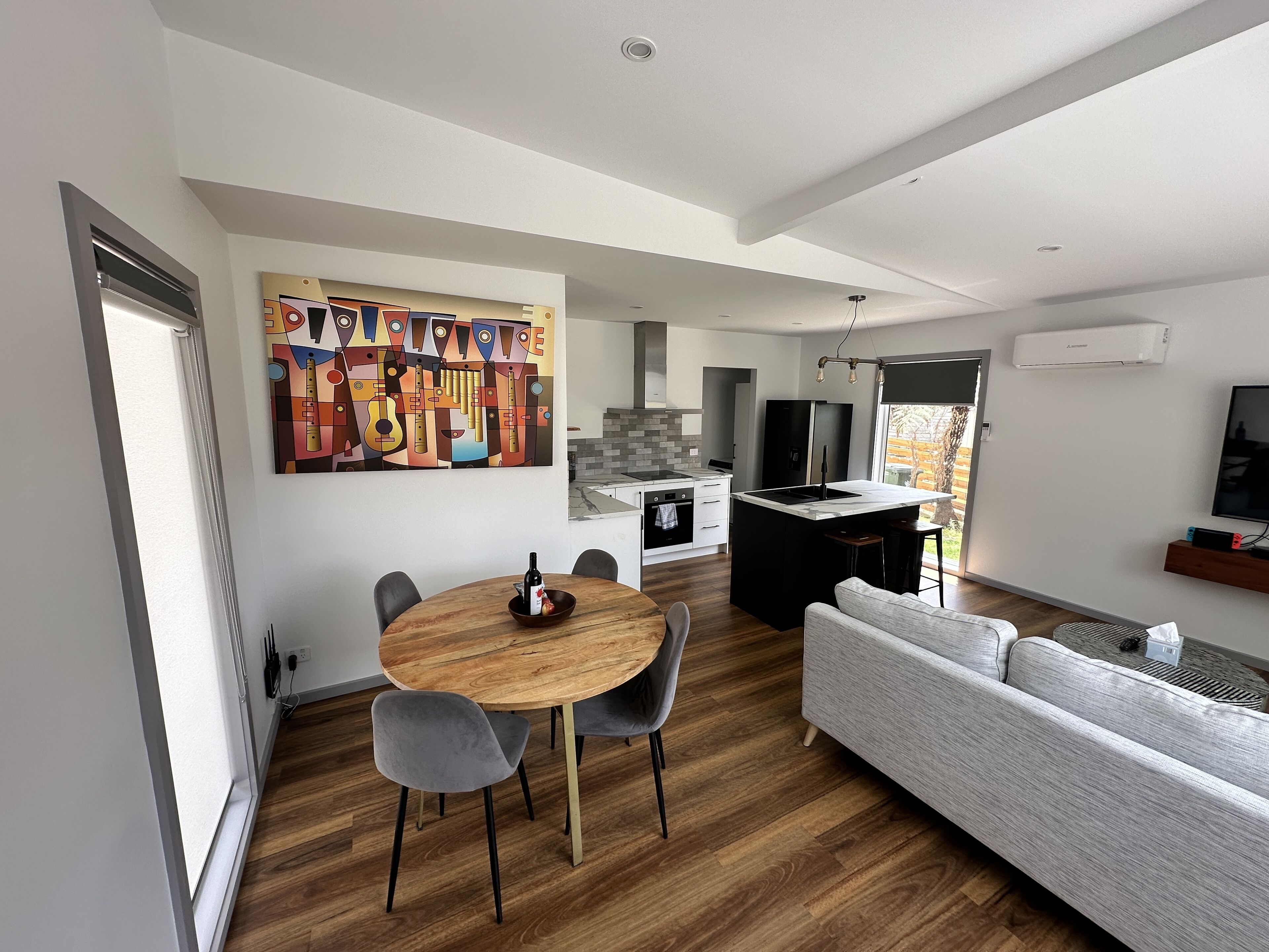 A modern kitchen with a central island, a dining area with a wooden table and grey chairs, and a grey sofa.
