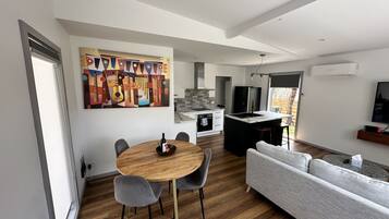 A modern kitchen with a central island, a dining area with a wooden table and grey chairs, and a grey sofa.