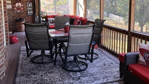 Une terrasse couverte avec une table et des chaises, un ventilateur de plafond et une vue sur l’extérieur.