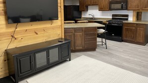 Una cocina moderna con gabinetes de madera, una estufa negra, un microondas y un televisor de pantalla plana grande montado en una pared de madera.