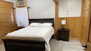 Un dormitorio con cama de madera, mesita de noche, lámpara y un calentador fijado a la pared.