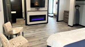 A hotel room with a bed, a TV mounted above a fireplace, a seating area with patterned chairs, and a walk-in closet. - Up North Luxury w/Unmatched Charm! 2 miles to MTU! (Hancock)