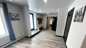 A spacious hallway with wooden flooring, a bench, and a door leading to another room. - Up North Luxury w/Unmatched Charm! 2 miles to MTU! (Hancock)