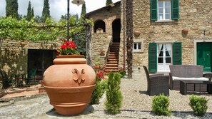A stone house with a large terracotta pot, outdoor seating, and a staircase leading to an upper level.