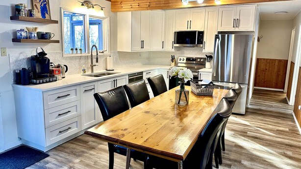 A modern kitchen with white cabinets, stainless steel appliances, and a wooden dining table. - Cabin in Belair Properties (Bélair)