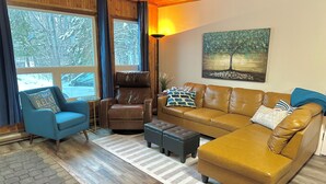 A cozy living room with a brown leather sofa, a blue armchair, and a brown recliner. There is a painting on the wall and a lamp on a side table. - Cabin in Belair Properties (Bélair)