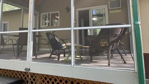 A covered outdoor seating area with a table and chairs, a wooden deck, and a view of a building with a door and windows. - Cabin in Belair Properties (Bélair)