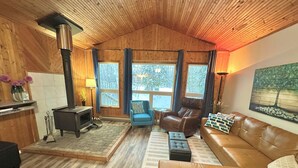 A cozy cabin interior with a fireplace, leather furniture, and large windows offering a view of the outdoors. - Cabin in Belair Properties (Bélair)