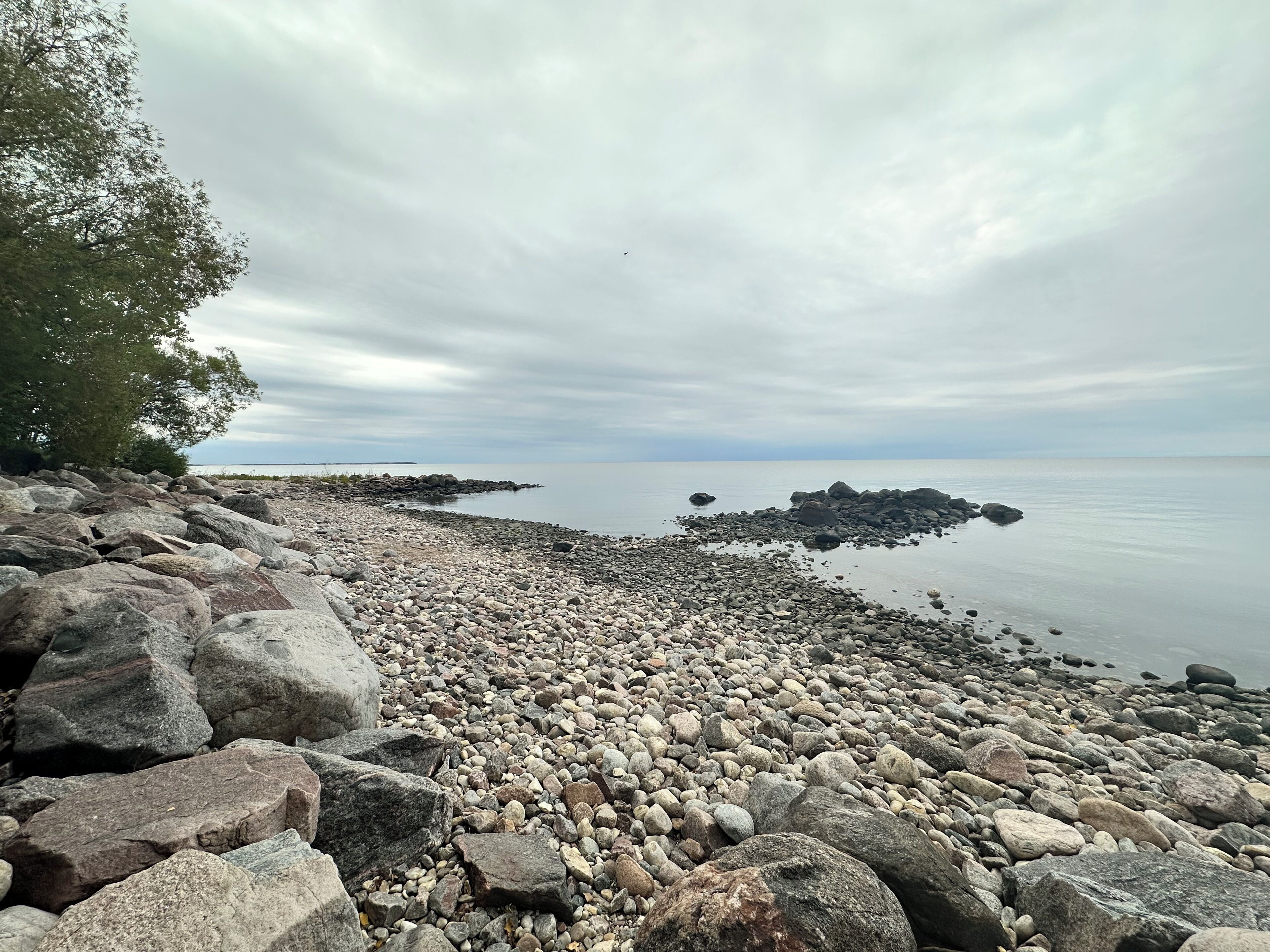A rocky shoreline with large boulders and a calm sea under a cloudy sky.