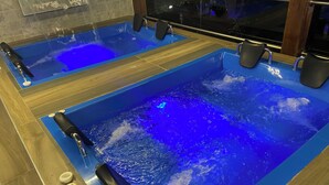 Dos tinas rectangulares con iluminación azul, suelo de madera y múltiples grifos.