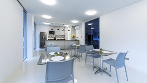 Una cocina moderna con armarios blancos, un refrigerador negro y un microondas. Hay una zona de comedor con una mesa y sillas, y un ventanal con vistas a la ciudad.