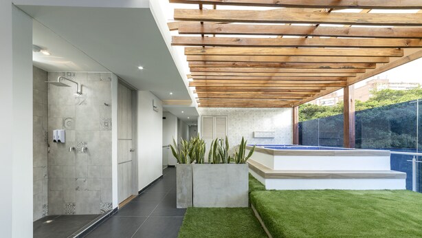 Un baño moderno con ducha, una jardinera de concreto con plantas y una zona de césped artificial verde.