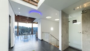 Un moderno vestíbulo de hotel con zona de ducha de vidrio, comedor con mesas al aire libre y vistas al exterior.