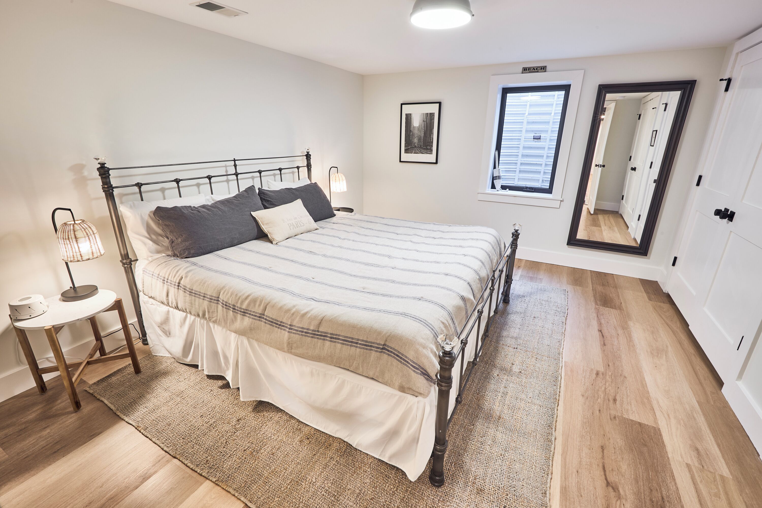 A bedroom with a bed, bedside table, lamp, and a mirror.
