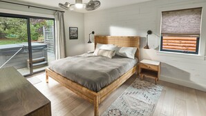 Ein Schlafzimmer mit einem großen Bett, einem Holzkopfende, Nachttischen, einem Fenster mit Jalousien und Blick auf eine Terrasse.