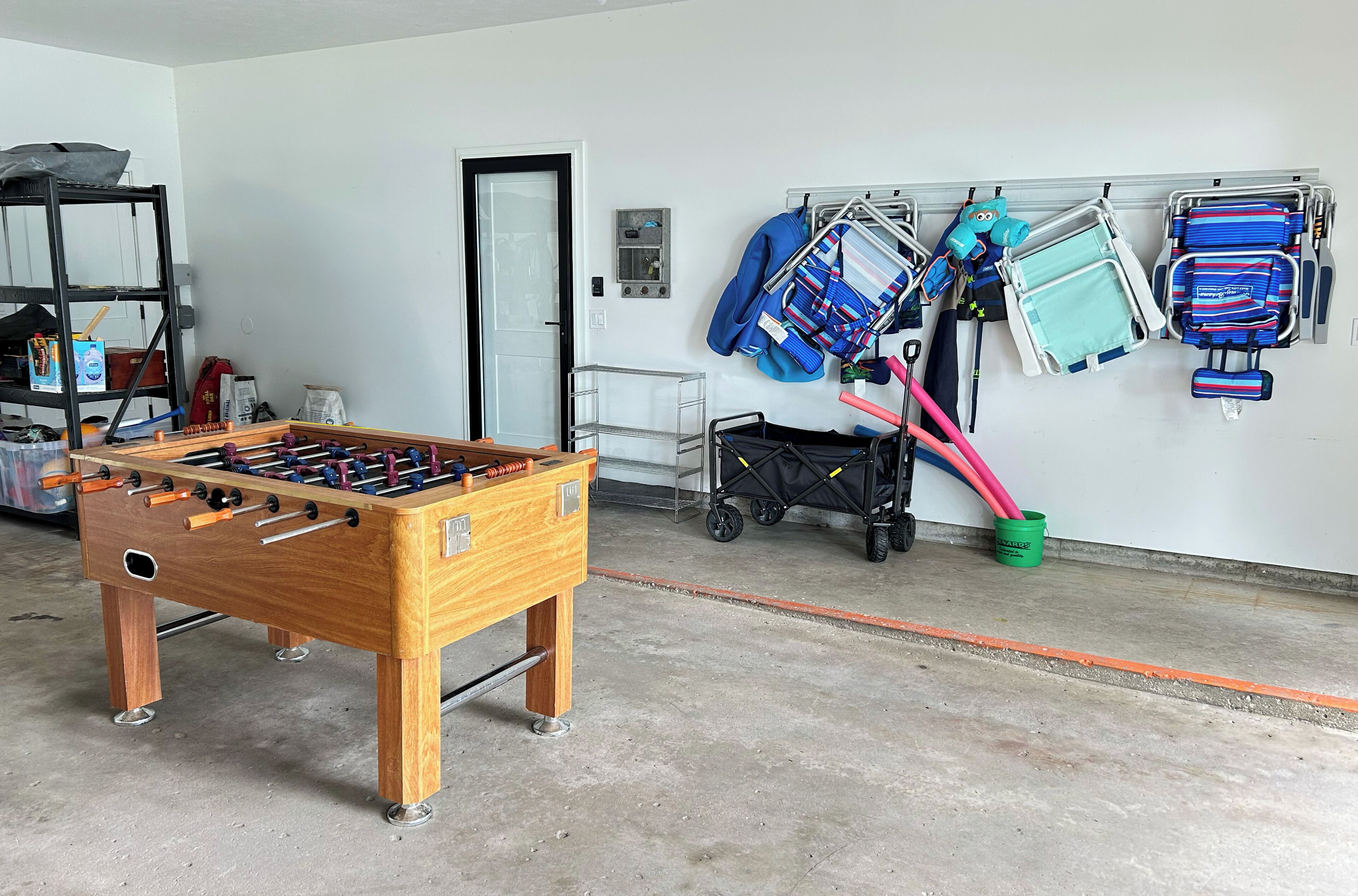 Een kamer met een tafelvoetbaltafel, een opslagrek met opgevouwen spullen, en een karretje met een kinderwagen.