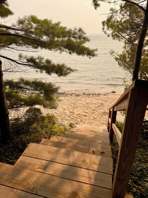 A wooden staircase leading to a sandy beach with pine trees framing the view.