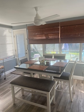 A dining area with a glass table, white chairs, a ceiling fan, and a view of the outdoors.