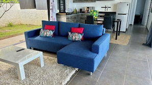 Una sala de estar moderna con un sofá azul, una mesa de centro blanca y una cocina al fondo.