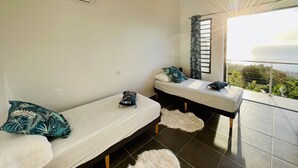 Una habitación con dos camas, una ventana con vista al mar y un ventilador de techo.