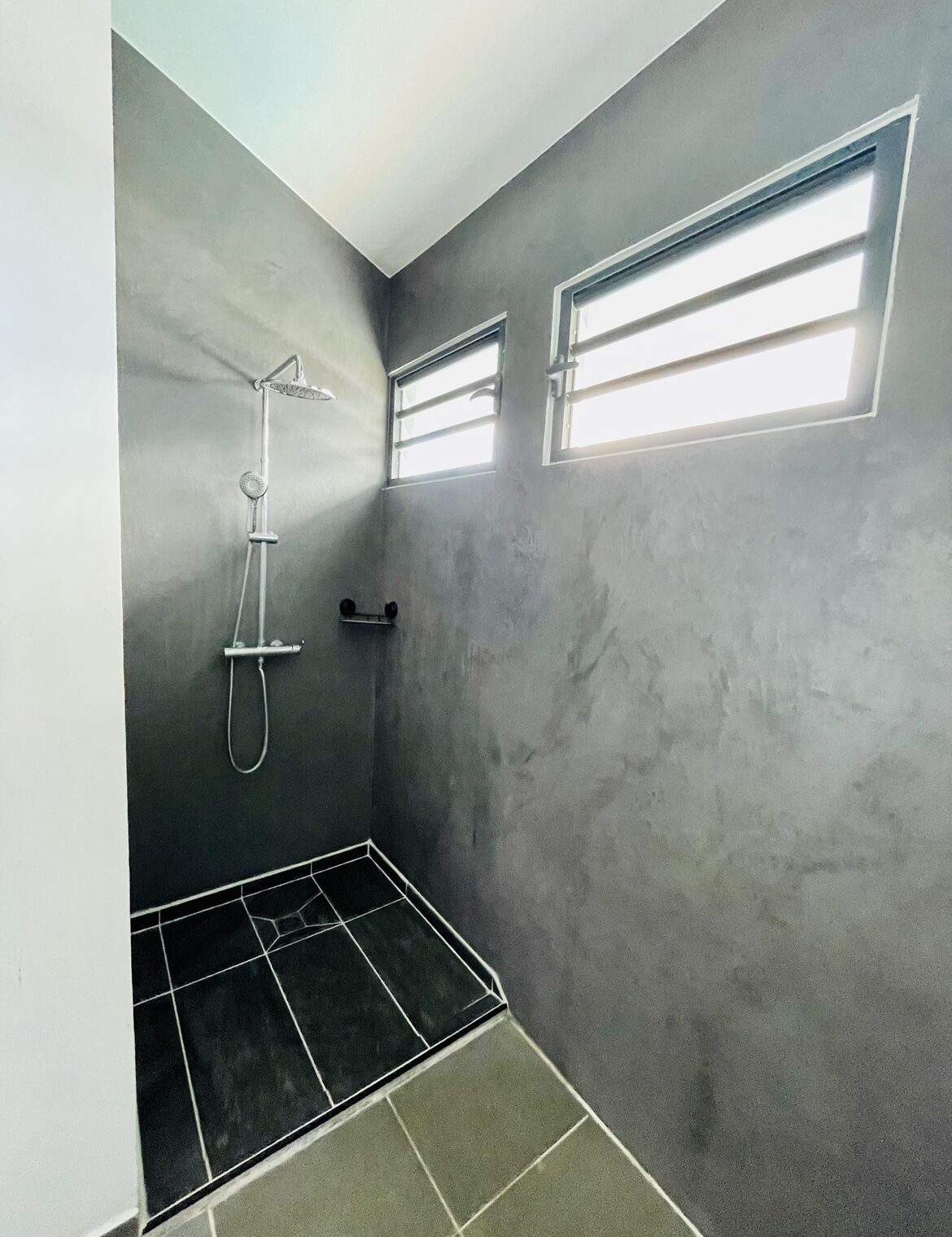 Un baño pequeño y tenuemente iluminado con ducha, toallero y ventana.