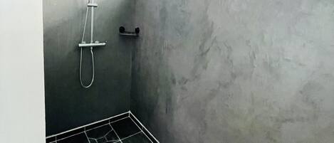 Un baño pequeño y tenuemente iluminado con ducha, toallero y ventana.