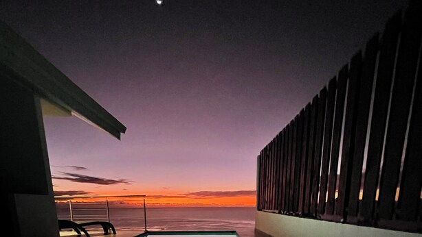 Una piscina con vistas al atardecer, la luna en el cielo y una barandilla a un lado.