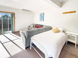 Ein Schlafzimmer mit Bett, einer Couch, einem weißen Nachttisch und einem Fenster mit Blick.