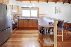 Eine Küche mit Holzausstattung, einem Edelstahlkühlschrank, einem Backofen, einer Spüle und einem Fenster mit Jalousien.