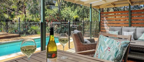 Uma área de estar coberta ao ar livre com piscina, uma garrafa de vinho e copos sobre uma mesa.