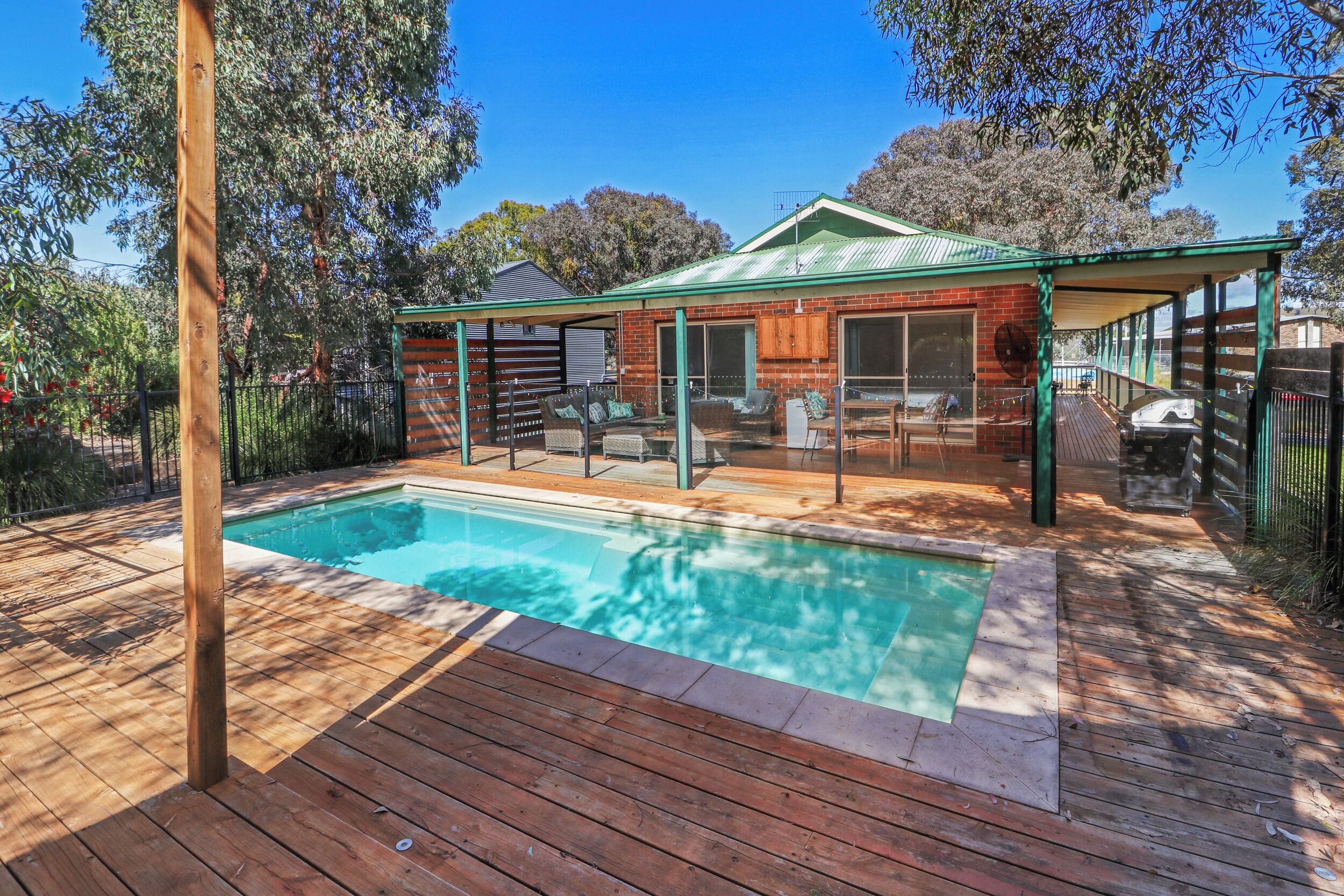 A backyard with a swimming pool, wooden deck, and a covered patio area.