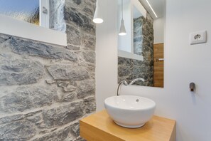 Une salle de bain avec un mur en pierre, un lavabo blanc et des luminaires suspendus.