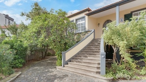 A cobblestone pathway leading to a house with a beige exterior and a red-tiled roof. - Casa Estufa 25 (Funchal)