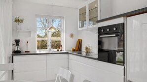 Cocina moderna con armarios blancos, horno empotrado y ventana con vistas a árboles.