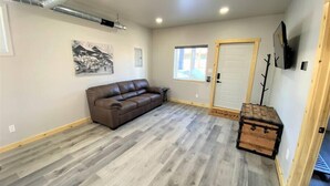 A spacious room with a brown leather sofa, a wooden chest, and a door. - Couples Getaway & Business Travel- 6 Miles to MTU (Chassell)