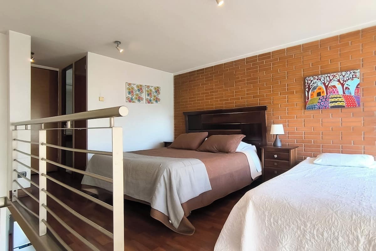 Quarto de hotel com cama, mesa de cabeceira, abajur e parede de tijolos.
