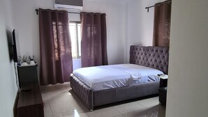 Quarto com cama, ventoinha no teto, televisão e uma pequena mesa.
