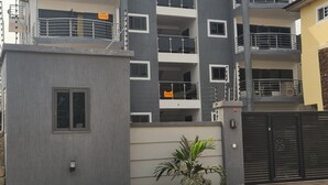 Um edifício residencial com vários andares, varandas, entrada com portão e uma pequena área de jardim.