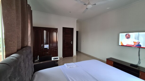 Quarto de hotel com cama, televisão, escrivaninha e guarda-roupa.
