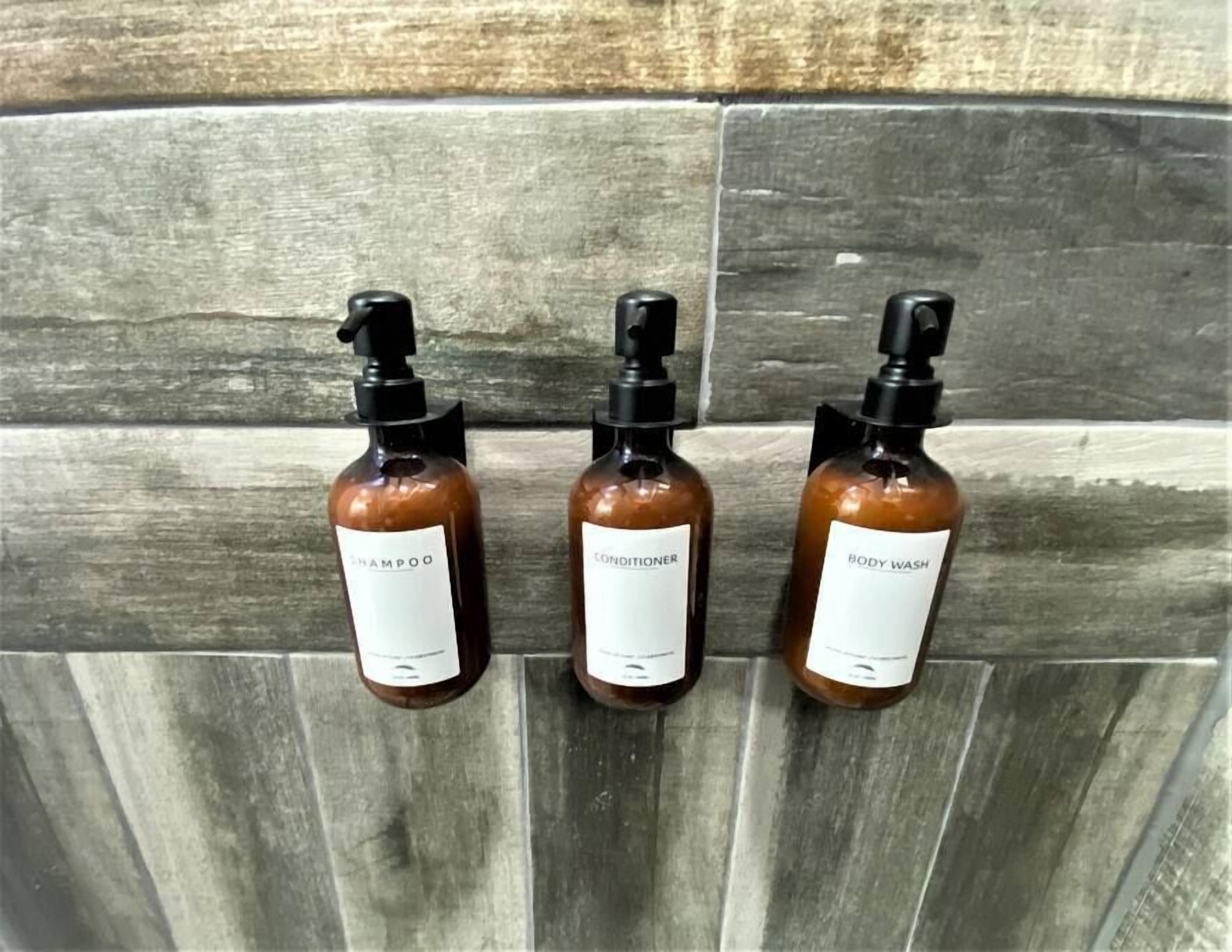 Three bottles of shampoo, conditioner, and body wash on a tiled wall.