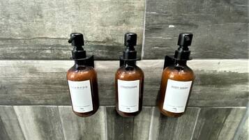 Three bottles of shampoo, conditioner, and body wash on a tiled wall.