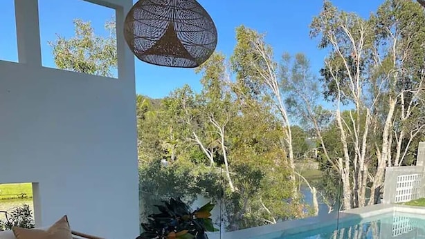 Un área de estar al aire libre con piscina, muebles de madera y vistas a árboles.